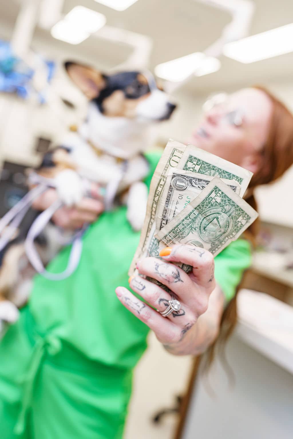 Vet tech in bright green scrubs holds a stack of dollar bills and a dog in the operating room