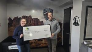 Dr. Kelly’s Surgical Unit donates to Apache Junction Animal Control. Pictured with a check in front of an Arizona landscape mural.