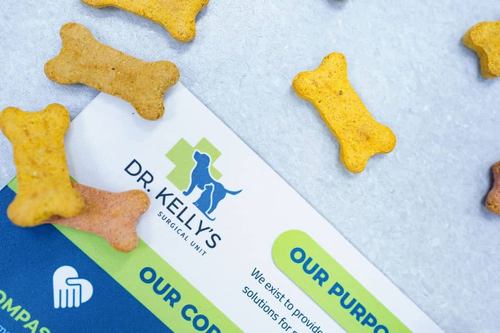 Dog bone-shaped treats scattered around a Dr. Kelly's Surgical Unit brochure highlighting their purpose and core values.